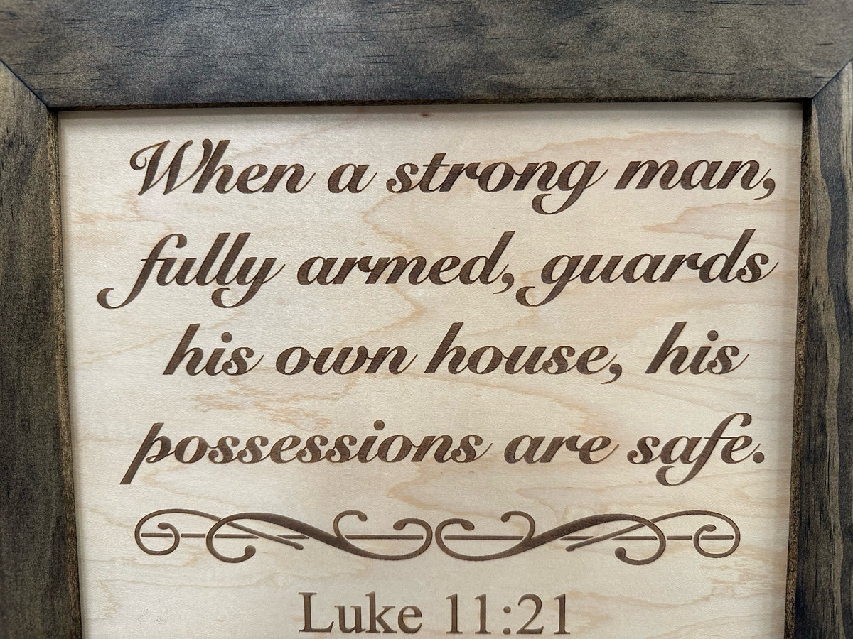 Wood-framed plaque with "When a strong man, fully armed, guards his own house..." from Luke 11:21 engraved in cursive.