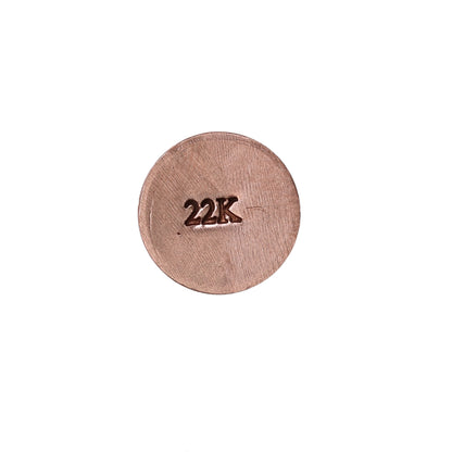 Close-up of a jewelers metal stamp demonstrating a 22K hallmark impression on a round copper-colored metal disc with white background