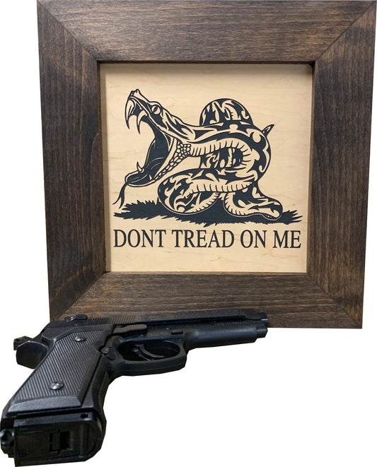 Wood-framed sign with "DONT TREAD ON ME" and a coiled snake graphic; a black handgun sits in front.