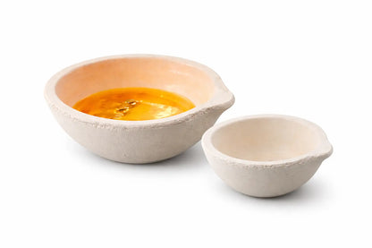 Front view of two ceramic crucible melting dishes, with gold-colored material in the larger dish on a white background