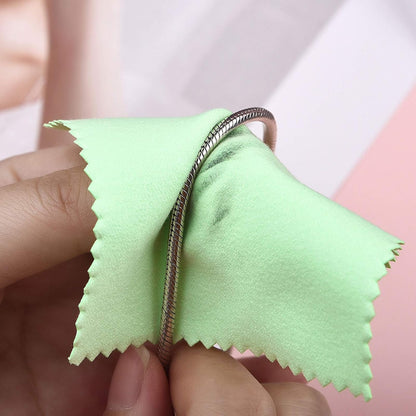 Hands polish a silver-toned chain with a green jewelry cleaning cloth against a pink background