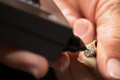 Close-up of an electronic diamond tester showcasing its probe testing a gemstone ring with hands holding the jewelry