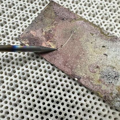 Close-up side view of Large 3MM Titanium Solder Pick With Wooden Handle showcasing its sharpened titanium tip against a metal sheet on a perforated soldering surface