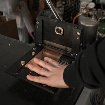 Front view of Pepetools 4-inch Guillotine Shear showing raised blade and cutting bed with a hand positioning a copper-colored sheet
