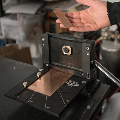 Front view of 4 inch Guillotine Shear showcasing a copper sheet, angle markings, and a hand-held metal strip in a workshop