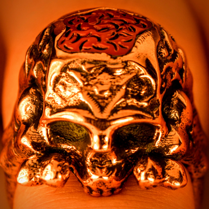 Copper-colored metal skull ring with an exposed brain design on top, worn on a finger.