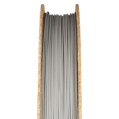 Close-up of M300 Tool Steel Filamet filament showcasing gray strands wound on a cardboard spool with a green background
