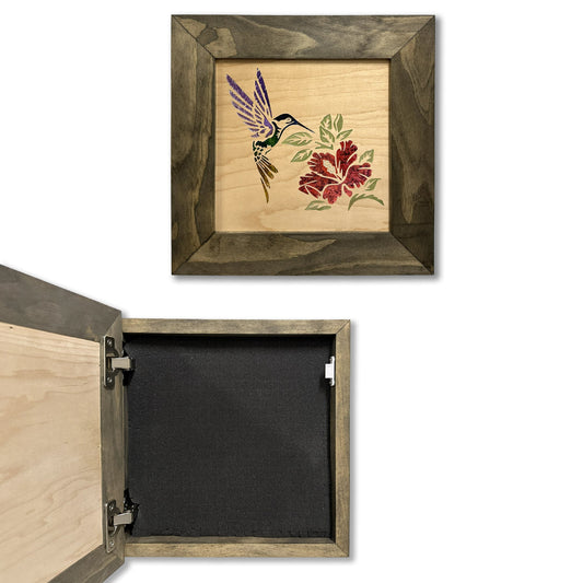 Square wooden wall safe with grey frame and a hummingbird and red flower marquetry design, shown open with a black foam interior.