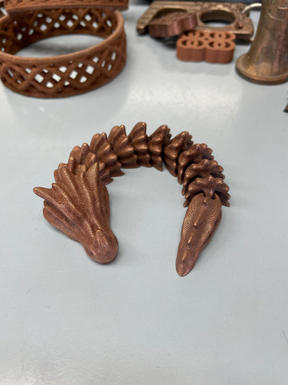 Copper-colored articulated dragon figurine with textured scales, displayed on a pale surface.