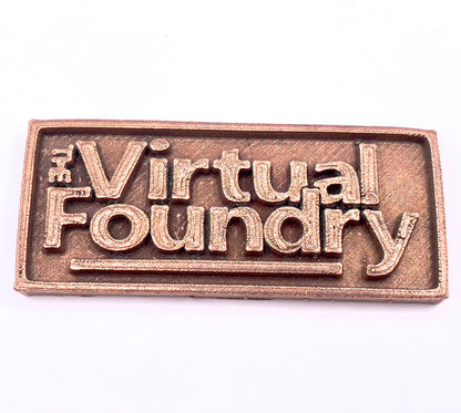 Copper-colored rectangular metal sign reading "The Virtual Foundry" in raised lettering.