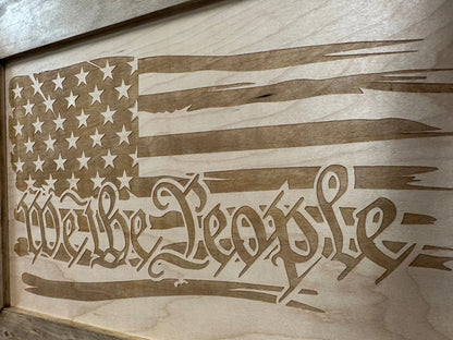 Close view of natural American Flag gun cabinet showcasing engraved We the People design with wood interior