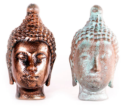 Two Buddha head statues: one polished copper-brown metal, the other with a weathered, oxidized green patina.