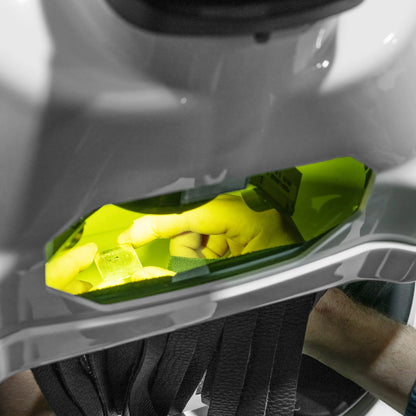 Hands positioning a metal workpiece beneath a green-tinted welding shield