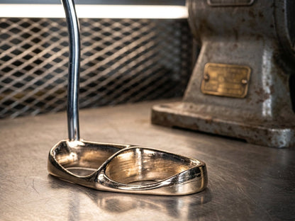 Close-up of a Bronze Filamet putter showcasing its reflective bronze-colored finish on a workshop bench