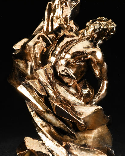 Polished gold-colored metallic sculpture of a human figure emerging from abstract, crystalline rock formations.