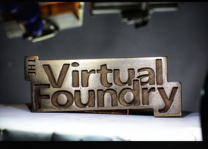 Metallic sign with carved text reading "The Virtual Foundry" in a blocky, angular layout.