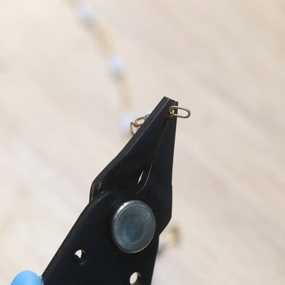 Close-up of Xuron grounded pliers for permanent jewelry welders showing black jaws and metal pivot on a light background