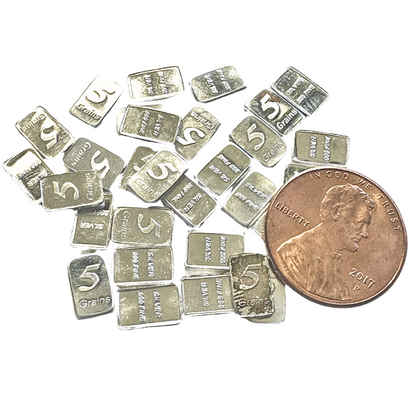Overhead view of solid silver bars marked 5 Grains and .999 Fine beside a penny for size comparison