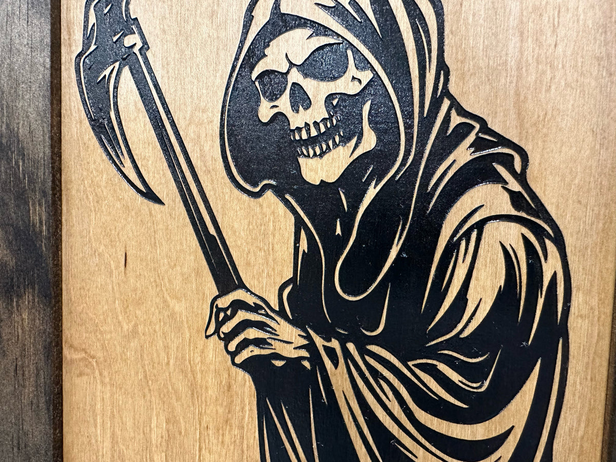 Black laser-engraved Grim Reaper holding a scythe on a light wooden plaque.