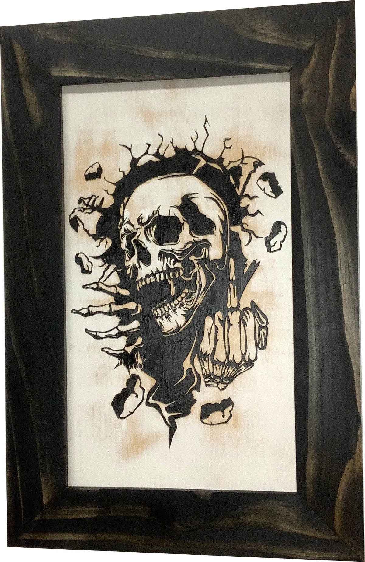 Black wood-framed art features a black-and-tan wood-burned skull breaking through a wall, giving the middle finger.
