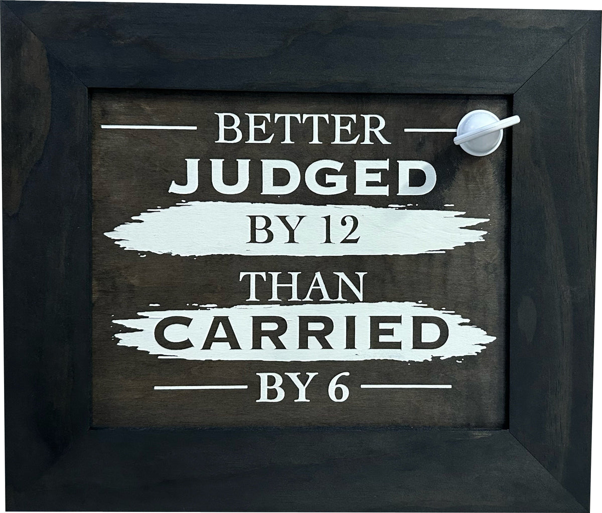A dark wooden sign with a black frame and white text that reads, "BETTER JUDGED BY 12 THAN CARRIED BY 6."