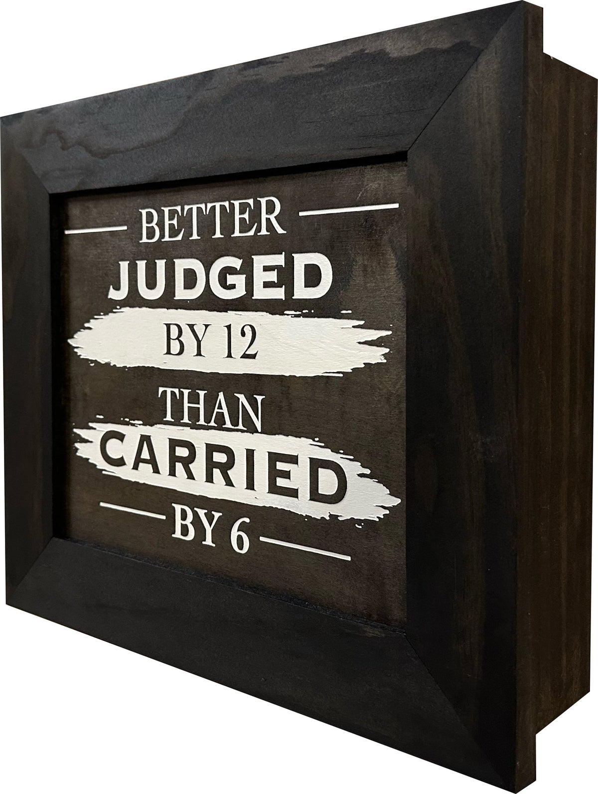 A dark brown wooden shadow box with white text reading "Better Judged By 12 Than Carried By 6."