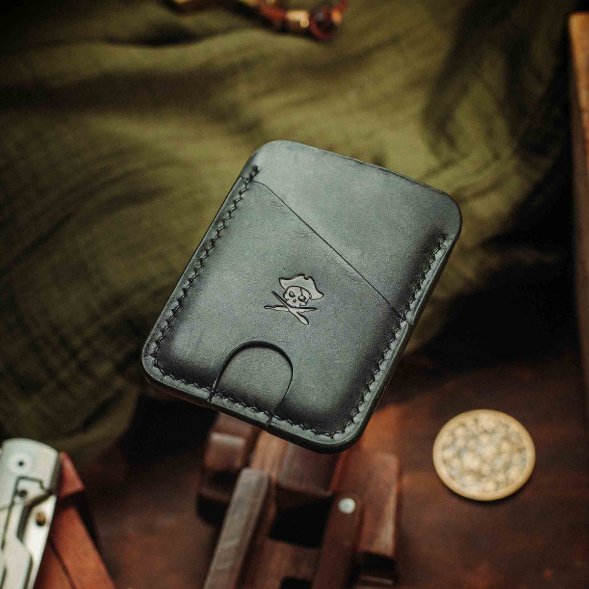 Front view of Boatswain v4 slim wallet showcasing black leather, stitched edges, and pirate skull emblem with workshop tools