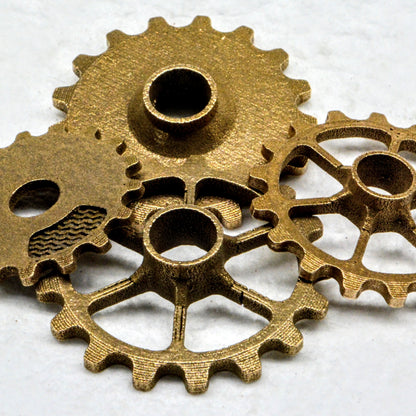 Four brass-colored metal gear test samples of varying designs, including solid and spoked wheels, overlap.
