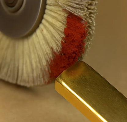 Close-up of ferric oxide red polishing compound powder on a polishing wheel beside a gold bar