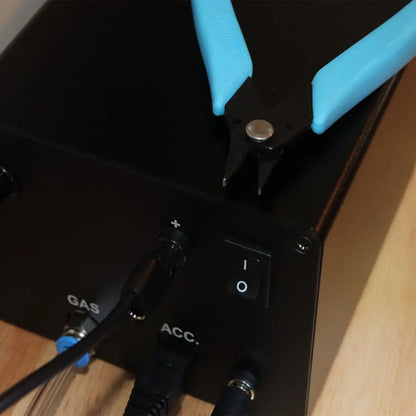 Close-up of Xuron grounded pliers for permanent jewelry welders showcasing blue handles and black jaws on black equipment