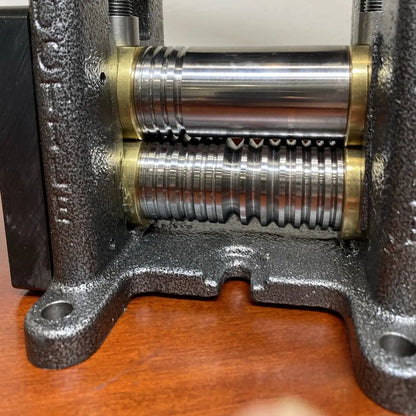 Close-up of a metal rolling mill showcasing textured rollers and a cast frame on a wooden surface