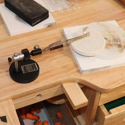 Angled view of Whaley Adjustable Third Hand showcasing its adjustable clamp arm and round work platform on a wooden workbench