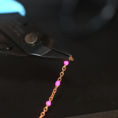 Close-up of Xuron grounded pliers holding a chain with pink beads against a black background
