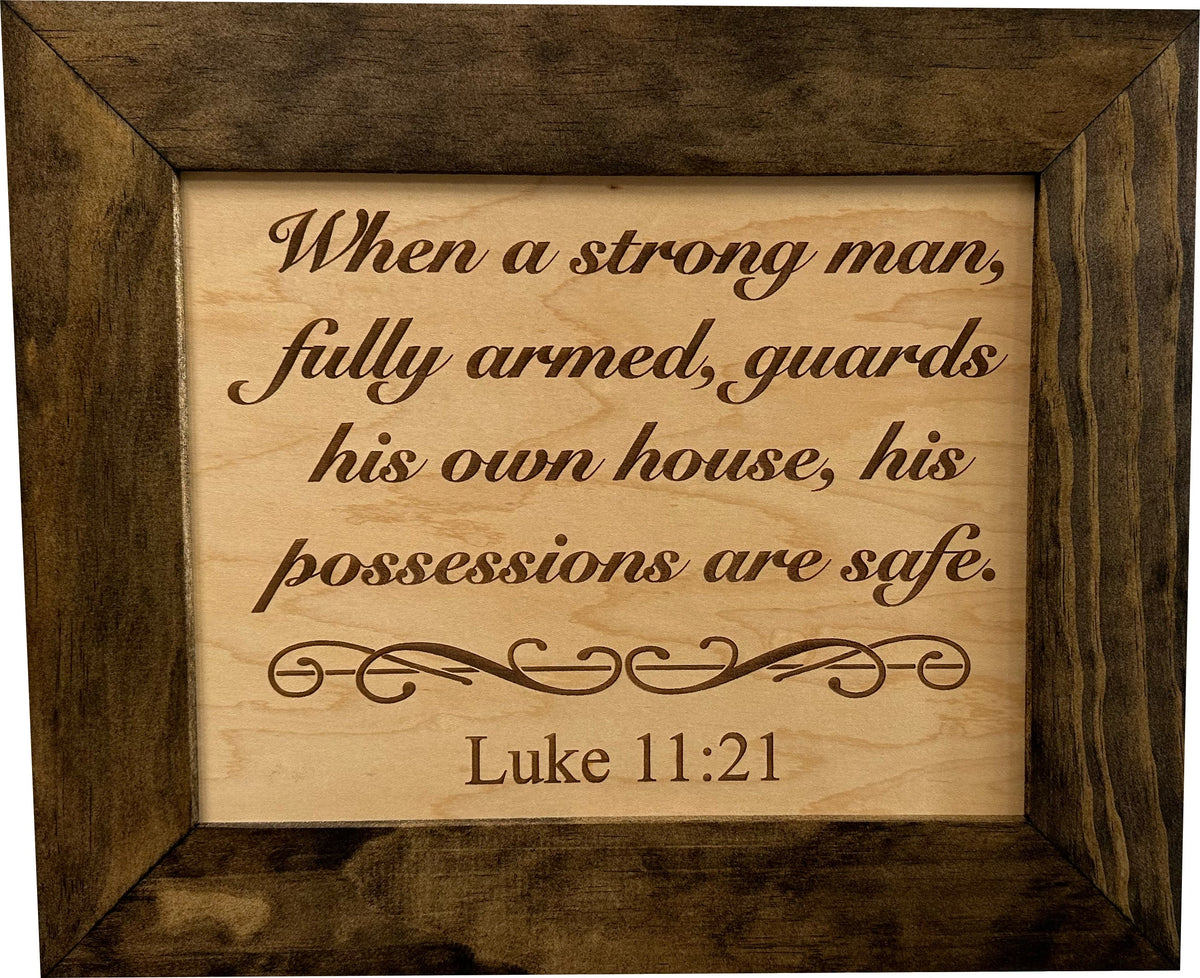 Wood-framed sign with the engraved Bible verse Luke 11:21 in brown script on a light wood background.